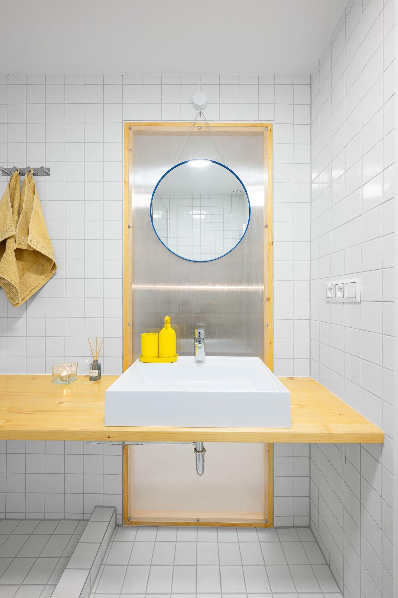 Badezimmer mit weißen Fliesen und Waschbecken auf einer Holzplatte