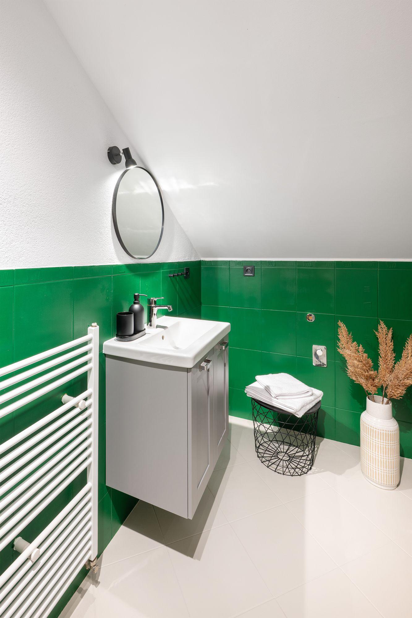 Badezimmer mit grünen Fliesen, Waschbecken und rundem Spiegel
